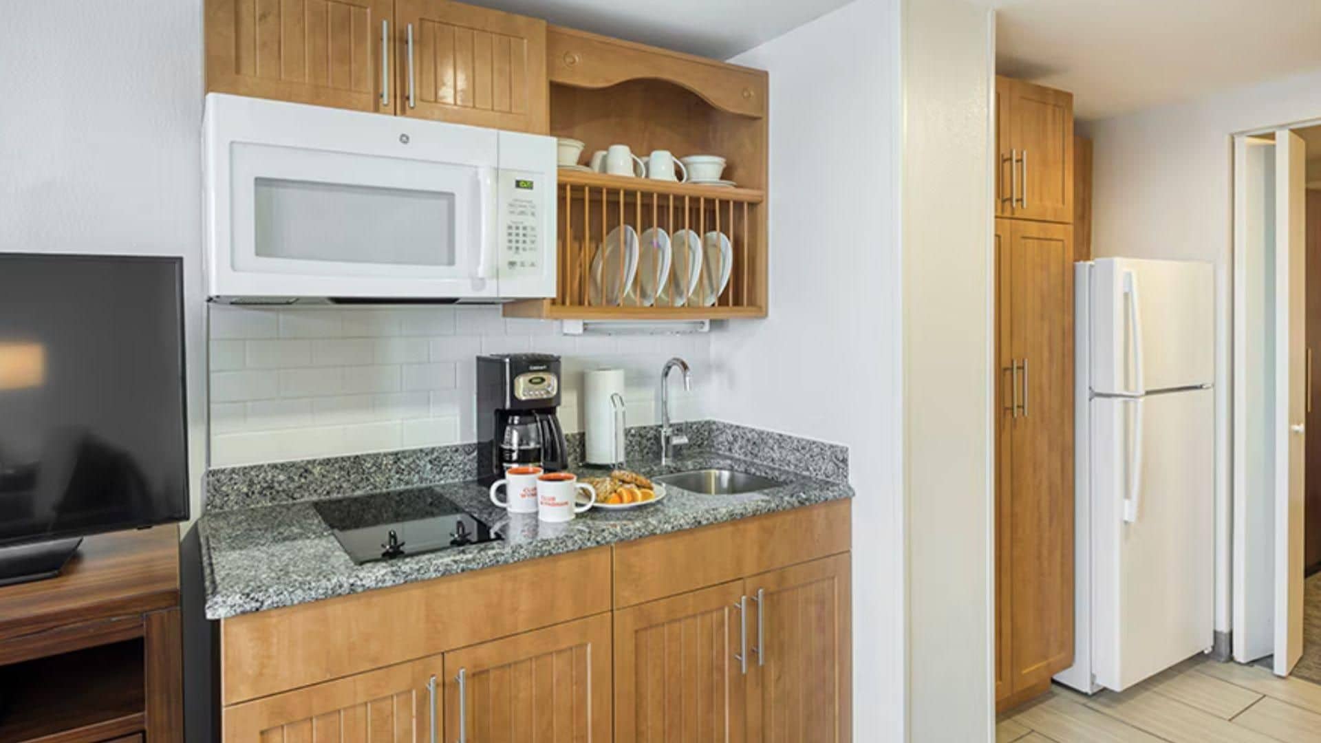 A kitchen with wooden cabinets, a microwave, a coffee maker, and a refrigerator.