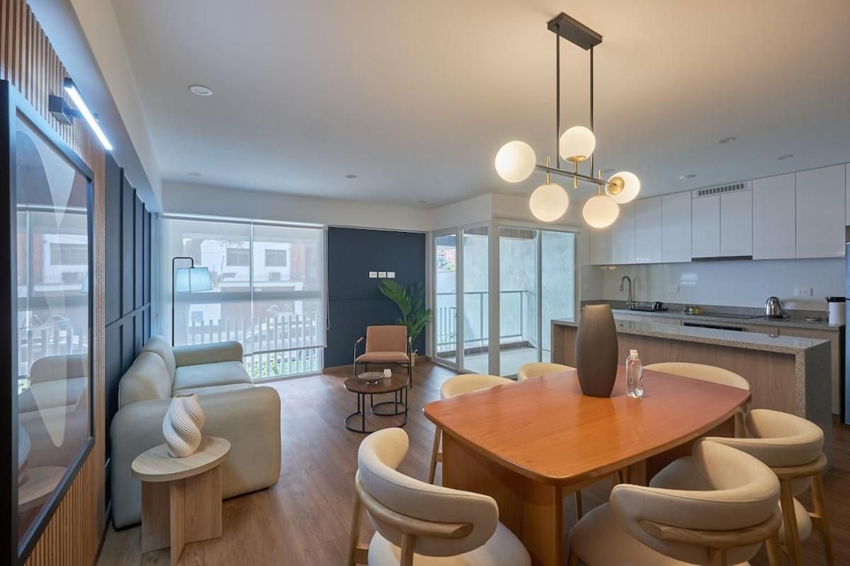 A modern kitchen with white cabinets, a wooden dining table, and a hanging light fixture.