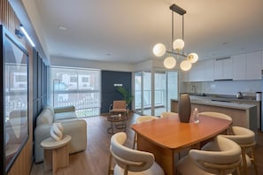 A modern kitchen with white cabinets, a wooden dining table, and a hanging light fixture. - Modern Acacias Spacious 2Br With Balcony, Steps From Larcomar (Miraflores)