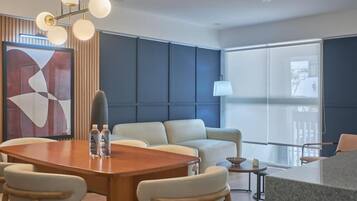 A modern hotel room with a large window, a dining table, and a sofa.