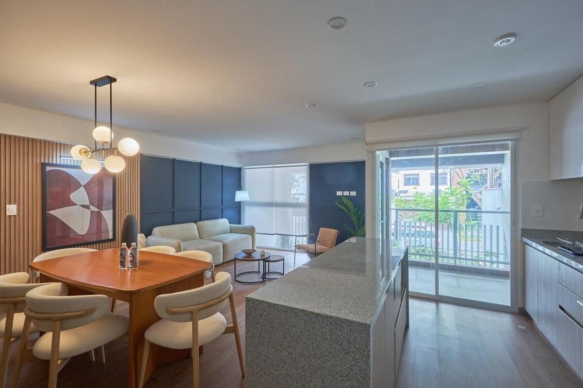 A modern kitchen with a granite countertop, a dining area with a wooden table and chairs, and a large window providing a view of the outside.