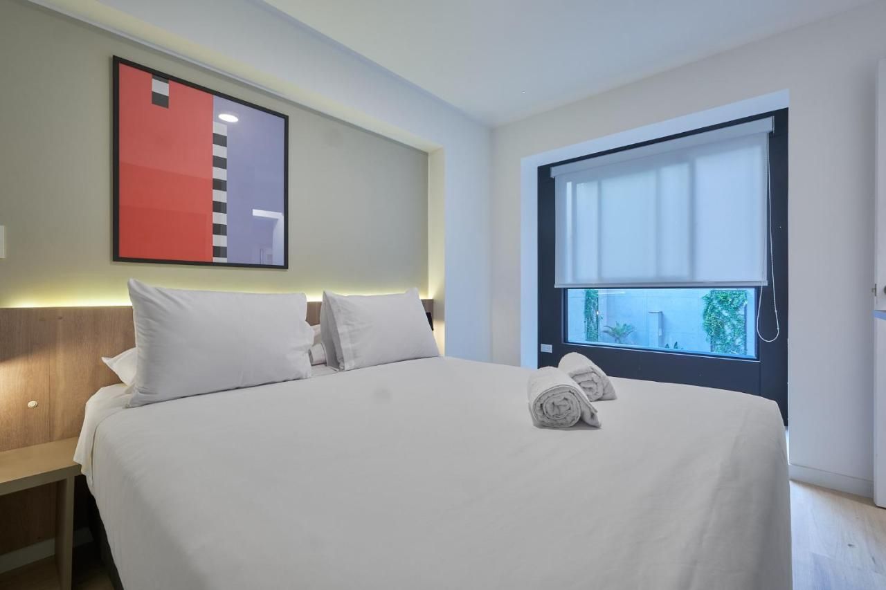 Habitación de hotel con cama, almohadas, mesita de noche, ventana con vista y una obra de arte en la pared.