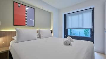 Habitación de hotel con cama, almohadas, mesita de noche, ventana con vista y una obra de arte en la pared.