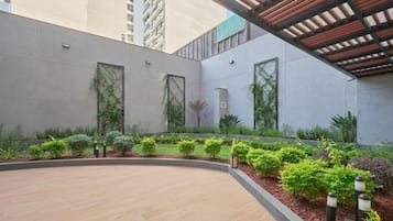 Un patio con un sendero curvo, una pérgola y diversas plantas.