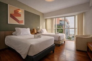Ein Hotelzimmer mit zwei Betten, einem Schlafsofa, einem großen Fenster und einem gerahmten Kunstwerk an der Wand.
