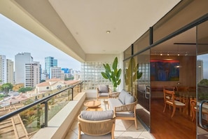 Ein Balkon mit Blick auf die Stadt, ausgestattet mit Korbstühlen und einer Couch, sowie ein Essbereich mit Holzsesseln und einem Glastisch.