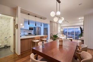 A modern kitchen with a central island, pendant lighting, and a dining area with a large table and chairs. - Pardo 510 Suites By Geko (Miraflores)