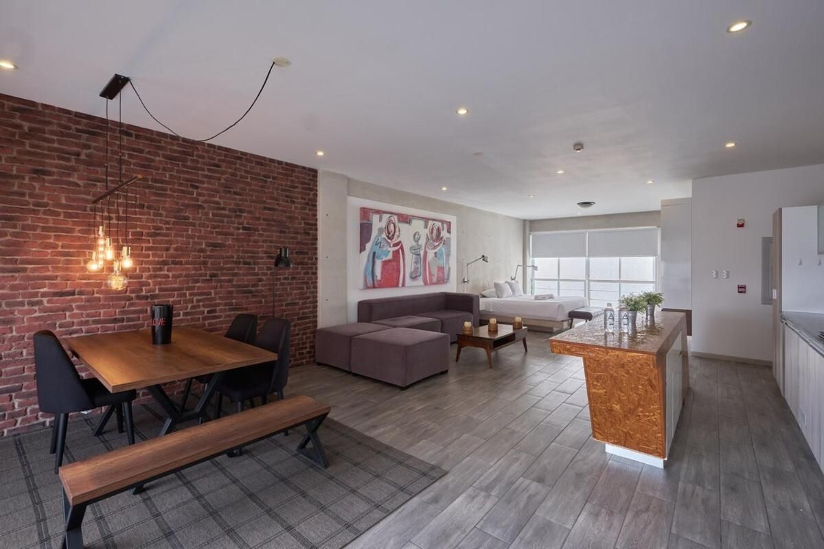 A modern living space with a dining area, a sofa, a kitchen island, and a brick accent wall.
