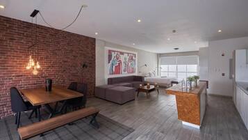A modern living space with a dining area, a sofa, a kitchen island, and a brick accent wall.