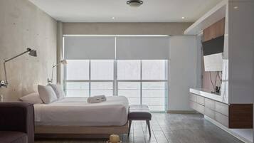 A modern bedroom with a large bed, bedside lamps, a bench, and a view through a large window.