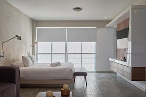 Ein modernes Schlafzimmer mit einem großen Bett, Nachttischlampen, einer Bank und Blick durch ein großes Fenster.