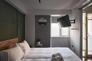 A bedroom with a bed, a round mirror, a TV mounted on the wall, and a window. - San Martín 207 Barranco Residences By Geko (Barranco)