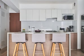 A modern kitchen with white cabinets, a microwave, a coffee maker, and three bar stools. - Stylish Inclán 343 Apartment By Geko (Lima)