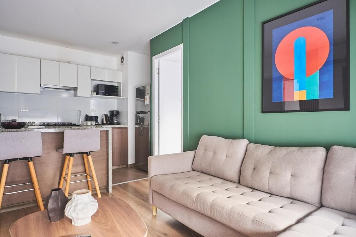 A modern kitchen with white cabinets, a dining area with a grey sofa, and a green accent wall.