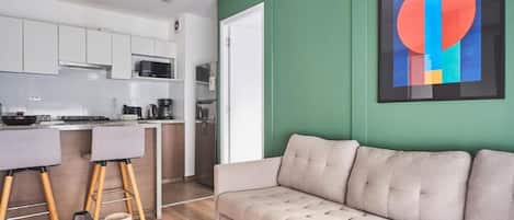 Eine moderne Küche mit weißen Schränken, ein Essbereich mit grauem Sofa und einer grünen Akzentwand.