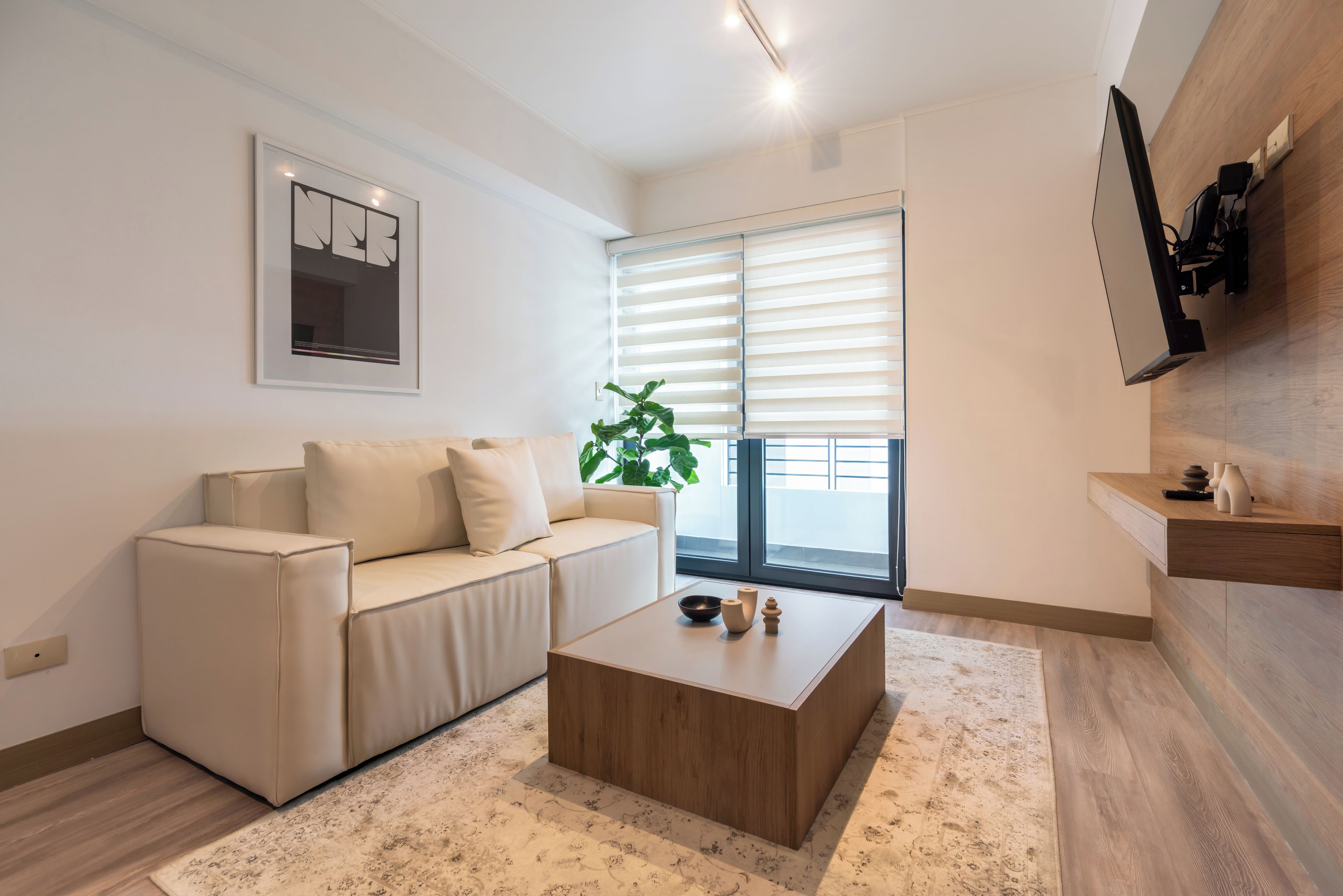 A modern living room with a sofa, a coffee table, a plant, and a window with blinds.