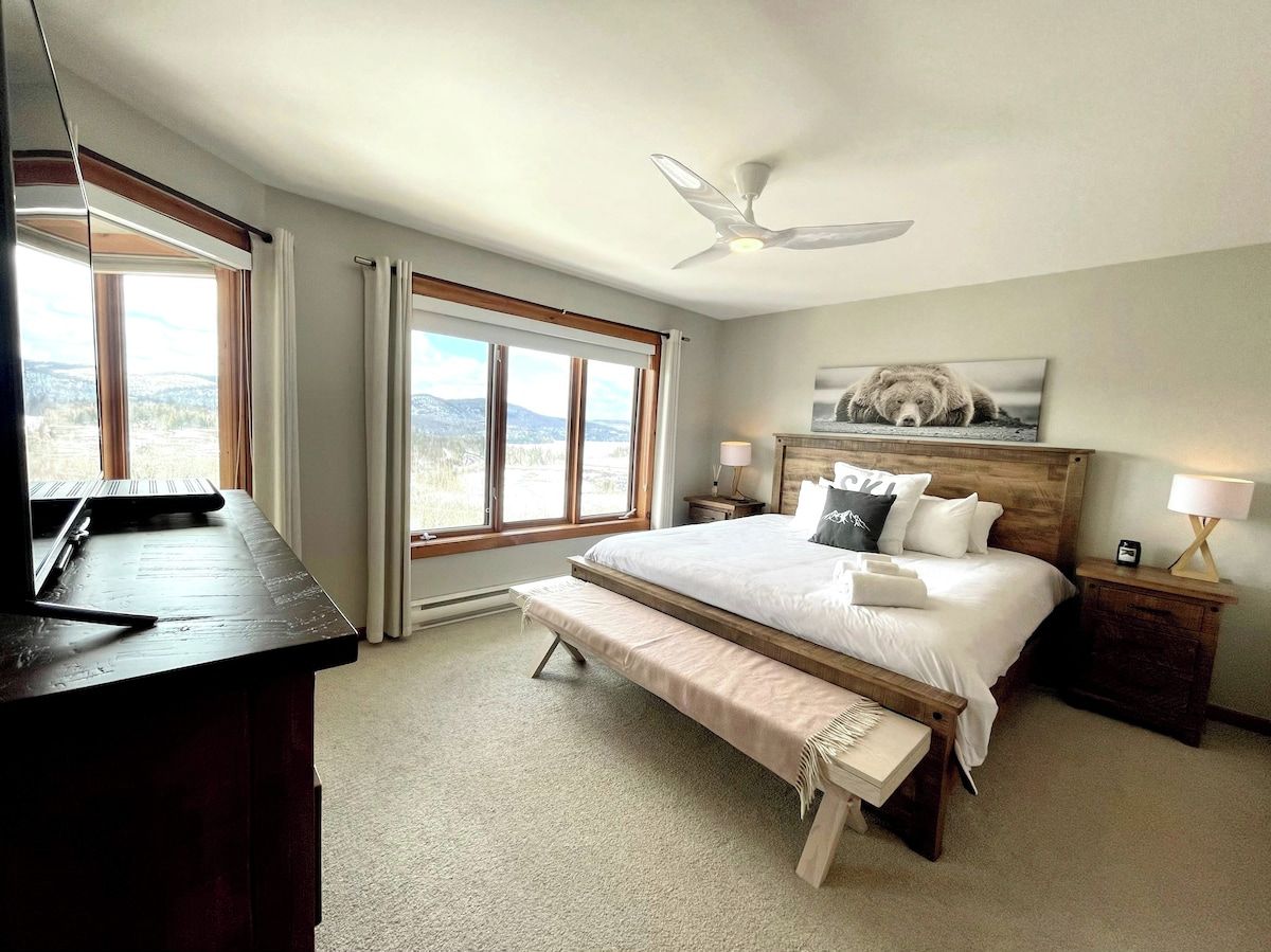 A bedroom with a bed, bench, bedside tables, and a ceiling fan.