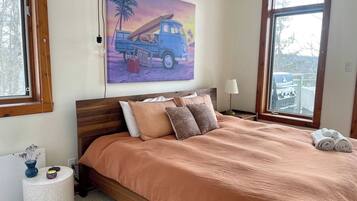 A bedroom with a bed, a painting, a lamp, and a window.