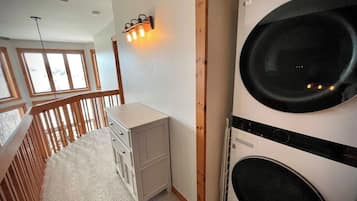 Une buanderie équipée d’un lave-linge, d’un petit placard et d’un escalier en bois.