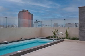 A rooftop swimming pool with a cityscape view, surrounded by a low wall and some greenery. - Aliaga Suites With Rooftop Pool In Magdalena (Magdalena del Mar)