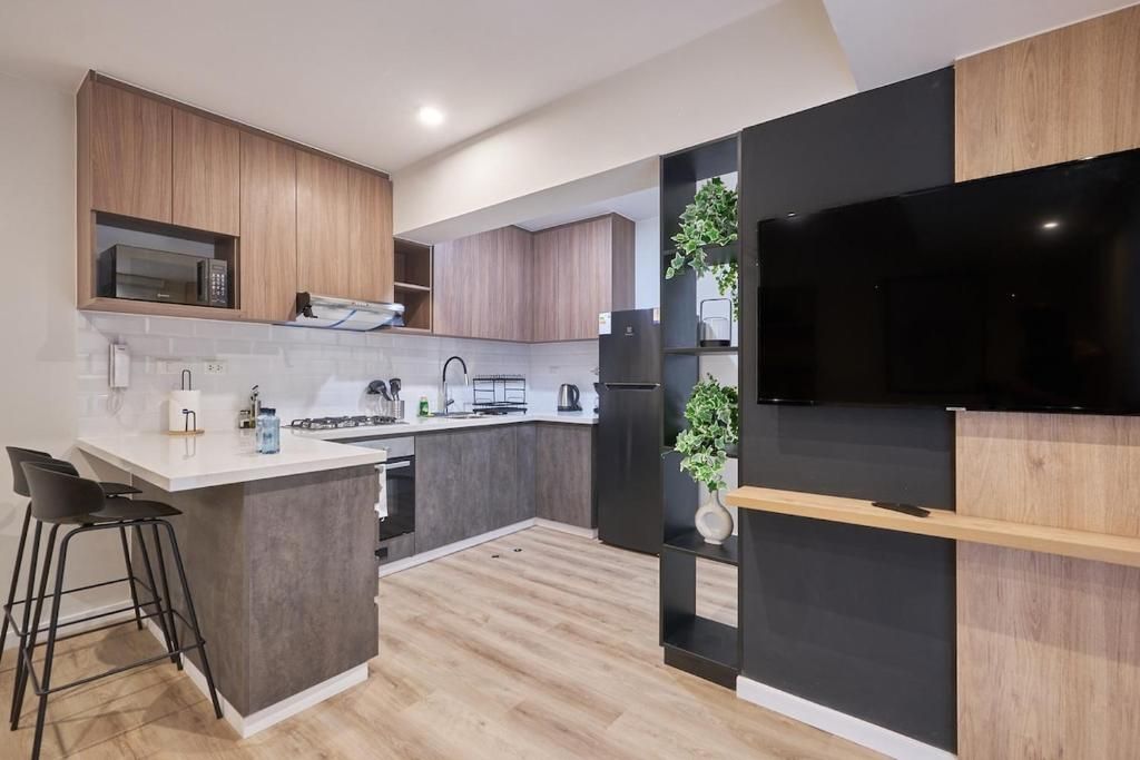 Una cocina moderna con una isla central, armarios de madera, un televisor negro y una planta.