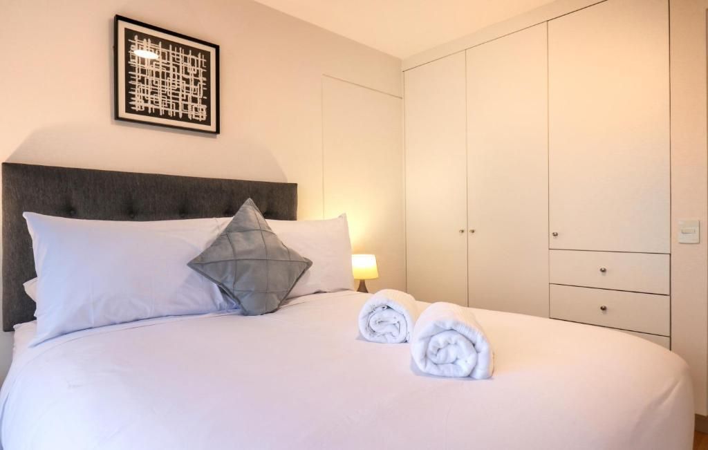 Habitación de hotel con cama, almohadas, una toalla doblada, mesita de noche con lámpara y armario.
