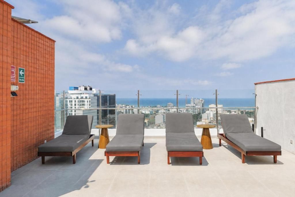 Un área de lounge en la azotea con cuatro sillones y pequeñas mesas redondas, con vistas a la ciudad y al mar.
