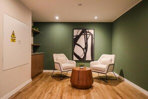 Una habitación con dos sillas blancas, una mesa de centro de madera y un cuadro abstracto grande en la pared.