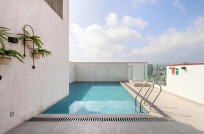 Una piscina en la azotea con cielo despejado, plantas en macetas y barandilla de cristal.