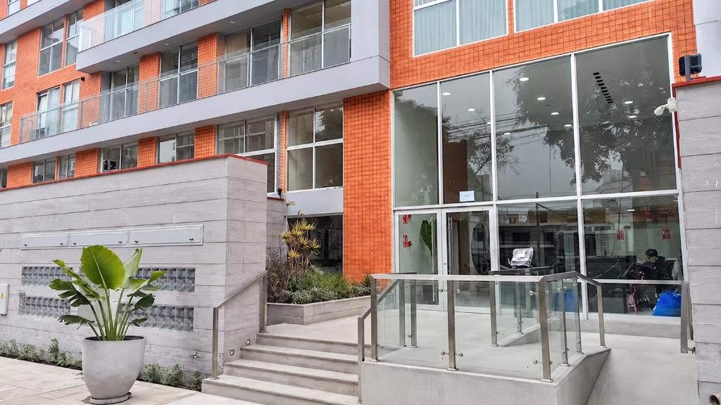 Un edificio moderno con fachada de vidrio, una escalera que conduce a una entrada protegida y una planta en maceta al frente.