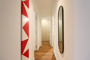 A hallway with a geometric wall design, a wooden floor, and a mirror on the right wall. - José Toribio Polo Residences By Geko (San Isidro)