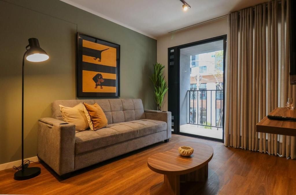 A modern living room with a sofa, a round coffee table, a floor lamp, a framed artwork, and a view through a glass door.
