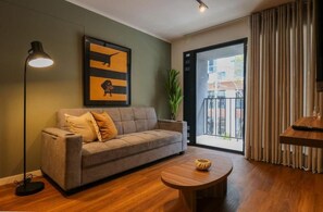A modern living room with a sofa, a round coffee table, a floor lamp, a framed artwork, and a view through a glass door. - José Toribio Polo Residences By Geko (San Isidro)