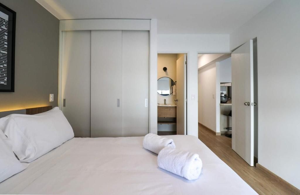 A hotel room with a bed, a wardrobe, a bathroom with a mirror, and a kitchenette.
