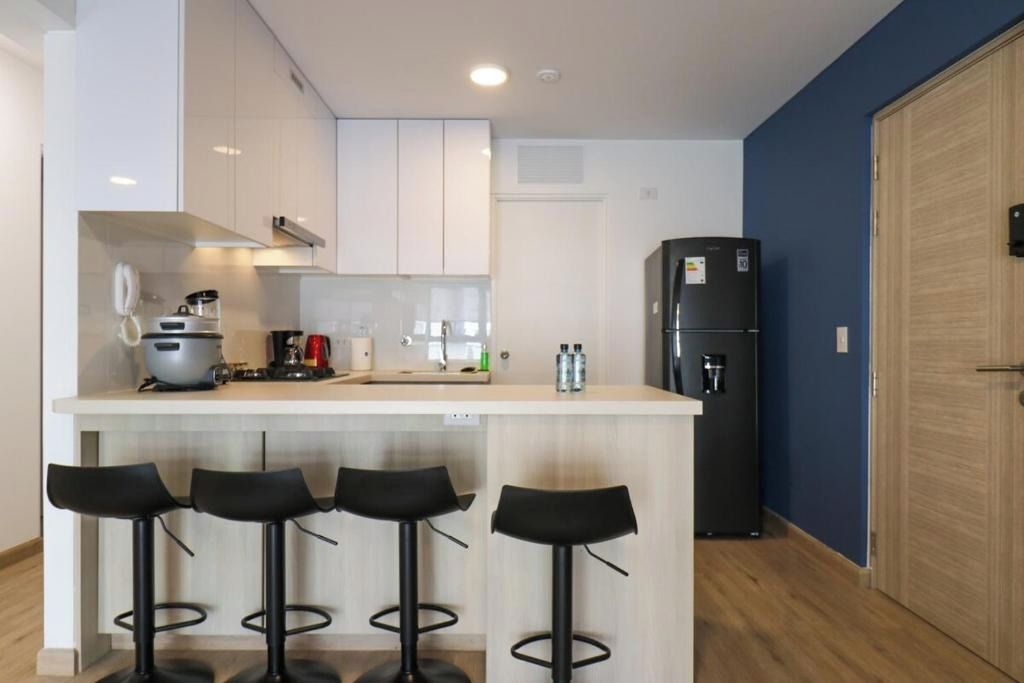 A modern kitchen with a central island, bar stools, a refrigerator, and a wooden door.