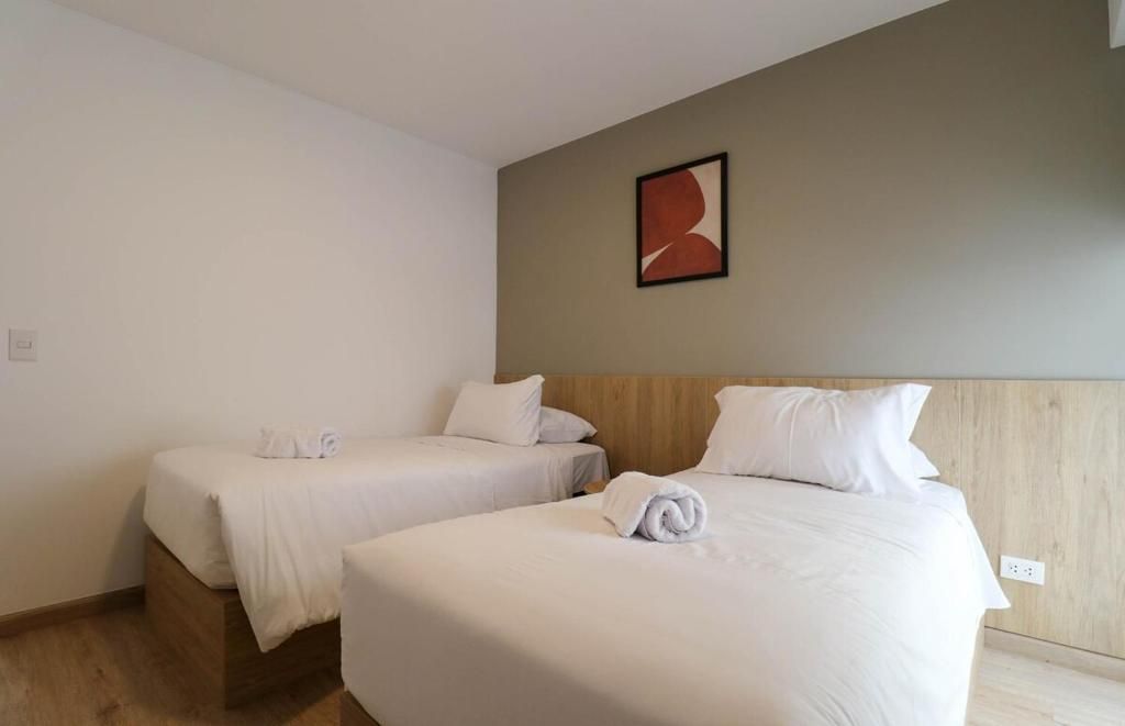Habitación de hotel con dos camas individuales, cabecero de madera, una obra de arte colgada en la pared y un enchufe.