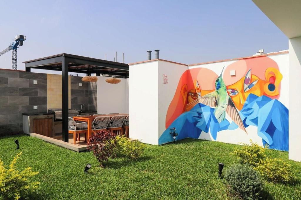 Un patio moderno al aire libre con zona de comedor, un mural y una grúa de construcción al fondo.