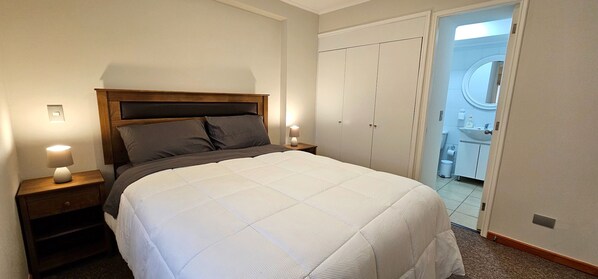 A bedroom with a bed, nightstands, a wardrobe, and a bathroom visible through an open door.
