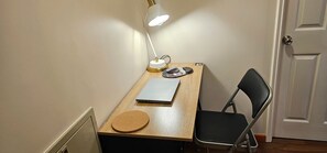 A small workspace with a desk, a laptop, a desk lamp, a chair, and a door.