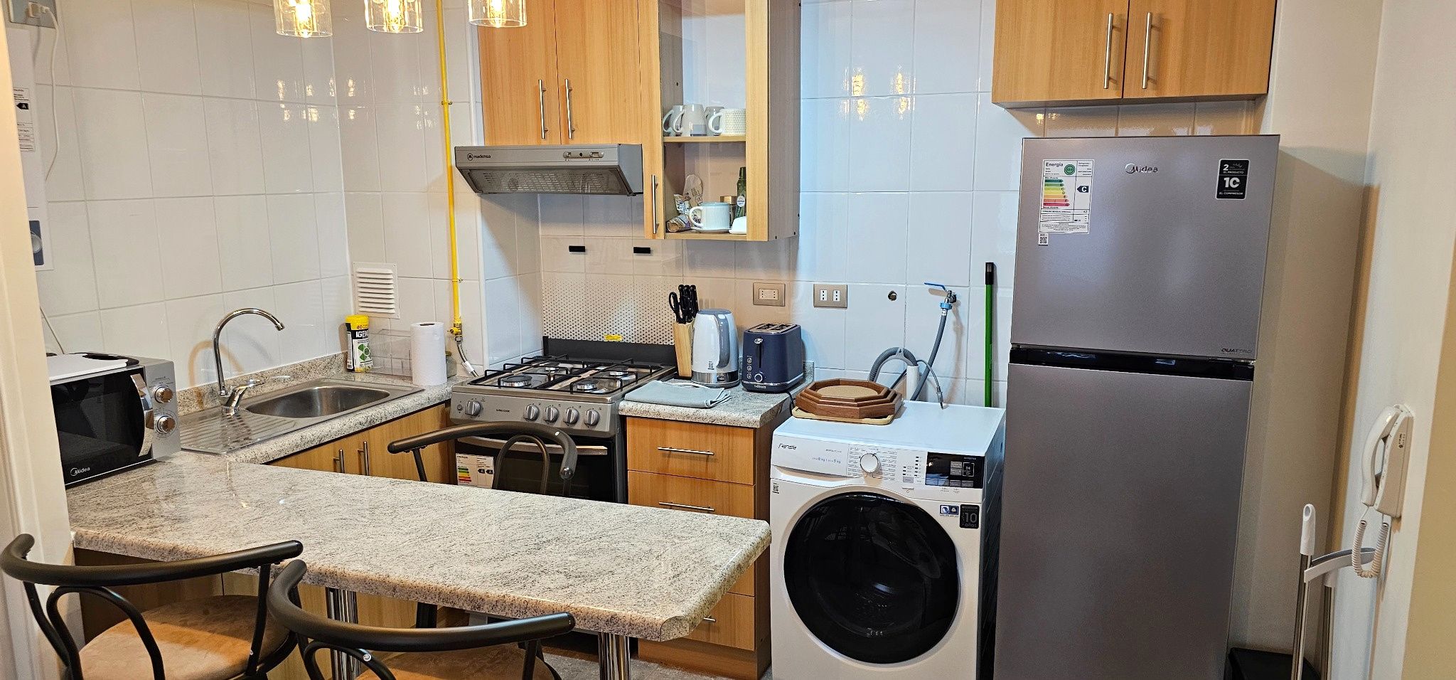 Une cuisine compacte équipée d’une cuisinière à gaz, d’un four à micro-ondes, d’un évier et d’un lave-linge encastré.