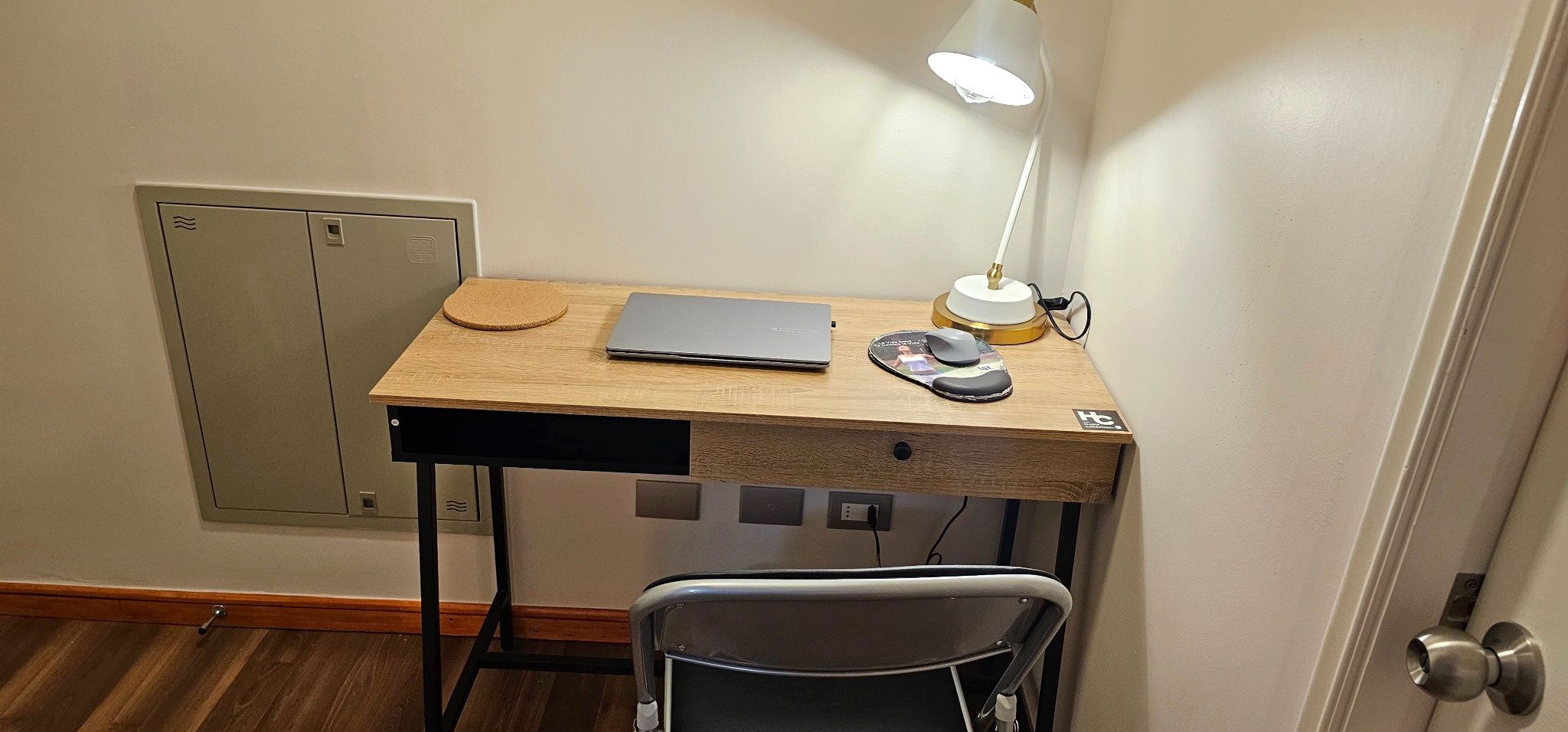 A compact workspace with a wooden desk, a laptop, a mouse, and a desk lamp.