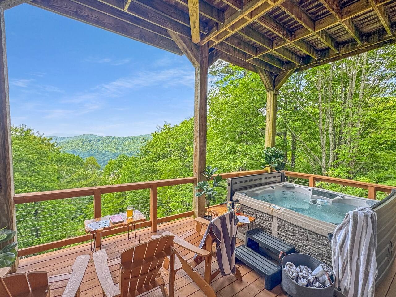Eine Holzterrasse mit Whirlpool, Sitzgelegenheiten im Freien und einem schönen Blick über ein bewaldetes Tal.