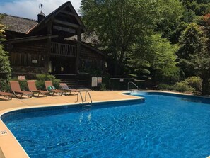 Ein Schwimmbecken mit Liegestühlen und einer Holzhütte im Hintergrund.