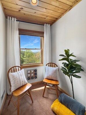 A room with two wooden chairs, a large window with curtains, a plant, and a yellow cushion. - Dreaming Tree Cabin; bike in/out, resort amenities (Mars Hill)