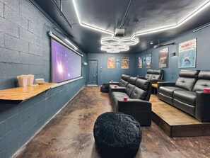 A modern home theater with a large screen, comfortable seating, and movie posters on the walls. - Dreaming Tree Cabin; bike in/out, resort amenities (Mars Hill)