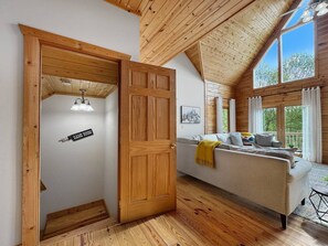 A room with a wooden ceiling, a sofa with cushions, a door labeled 'GAME ROOM,' and large windows. - Dreaming Tree Cabin; bike in/out, resort amenities (Mars Hill)