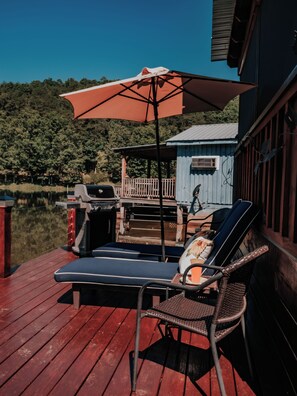 A deck with lounge chairs and a grill, overlooking a body of water and a dock. - The Lucky Lure is a beautiful two-bedroom cabin overlooking Johnson's Lake. (Rising Fawn)