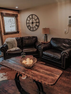 A living room with two leather sofas, a wooden coffee table with apples, a wall clock, and a lamp. - The Lucky Lure is a beautiful two-bedroom cabin overlooking Johnson's Lake. (Rising Fawn)