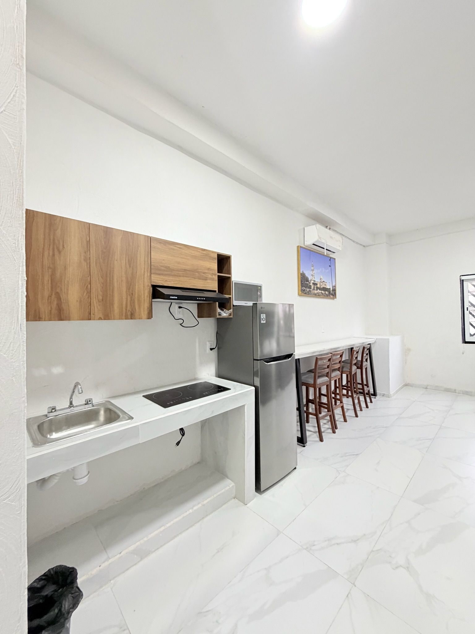 Una cocina moderna con encimeras blancas, un refrigerador de acero inoxidable, armarios de madera y una zona de bar con taburetes.