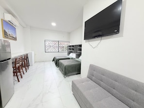 Ein kompakter Wohnraum mit Küchenzeile, einer Couch, zwei Betten und einem an der Wand befestigten Fernseher.